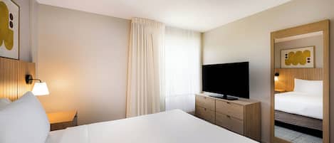 Habitación de hotel con una cama grande, un televisor sobre una cómoda de madera, un espejo y una lámpara fijada a la pared.