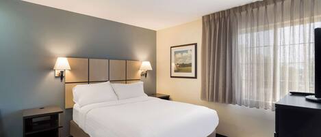 A hotel room with a bed, two bedside lamps, a nightstand, a TV, and a window with curtains.