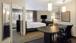 A hotel room with a bed, bedside table, lamp, TV, and a dining area with chairs and a table. - Sonesta Simply Suites Hampton (Hampton)