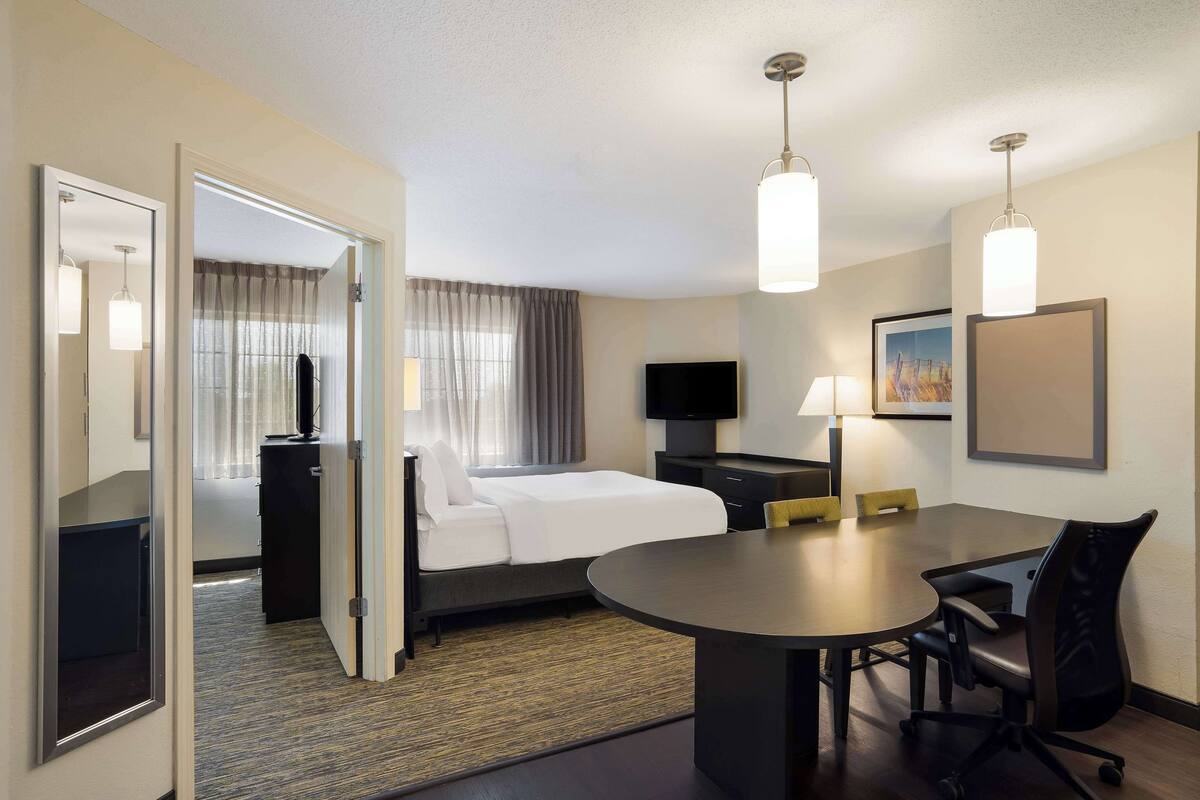 Une chambre d’hôtel comprenant un lit, une table de chevet, une lampe, une télévision et un coin repas avec des chaises et une table.