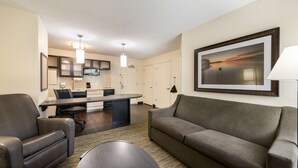 A modern living room with a gray sofa, a coffee table, and a dining area with a kitchen in the background. - Sonesta Simply Suites Hampton (Hampton)