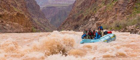 A group of people in a blue inflatable raft navigating through a river surrounded by steep canyon walls.