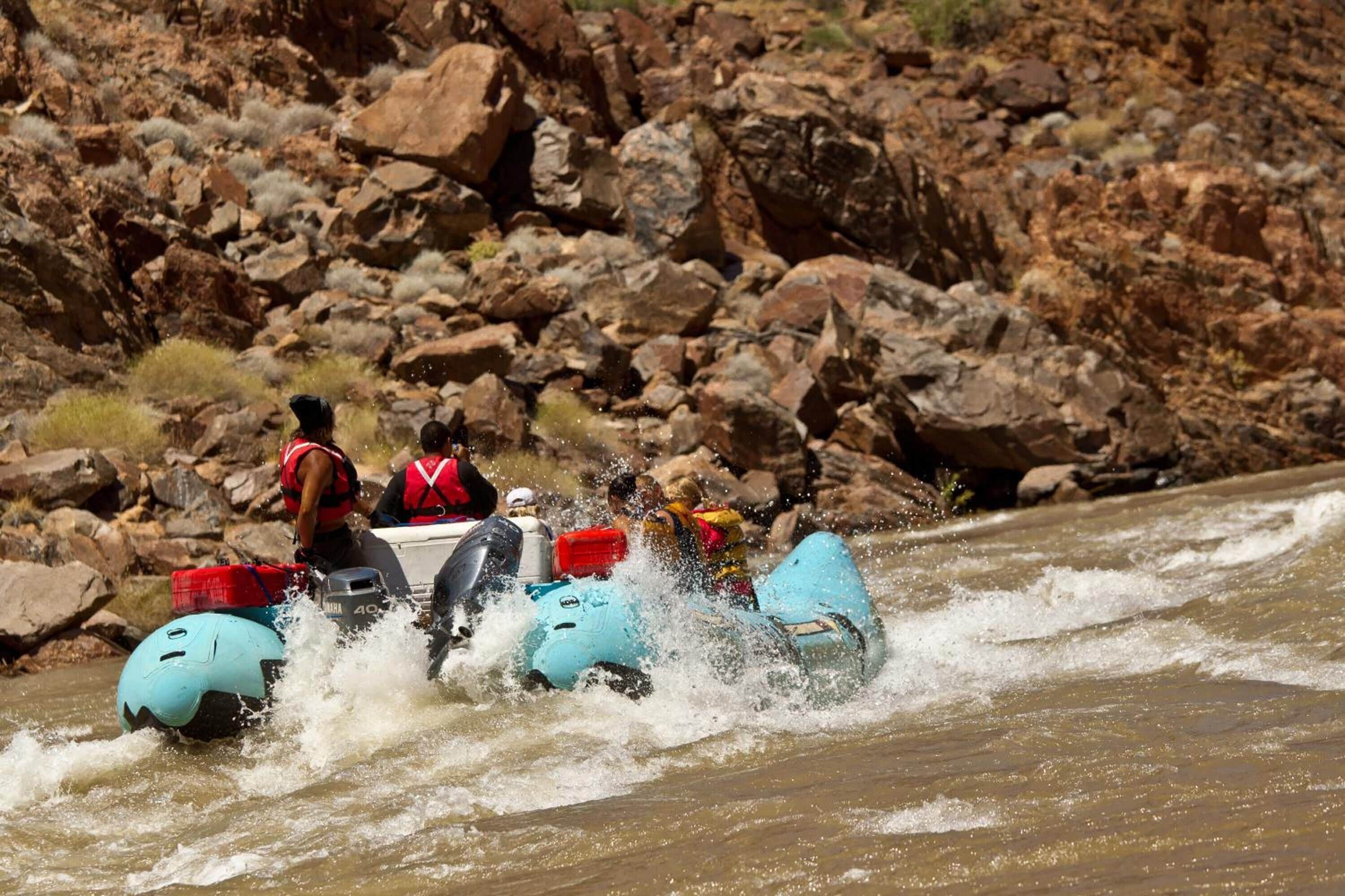 A group of people in a blue inflatable raft navigating through a river surrounded by rocky terrain.