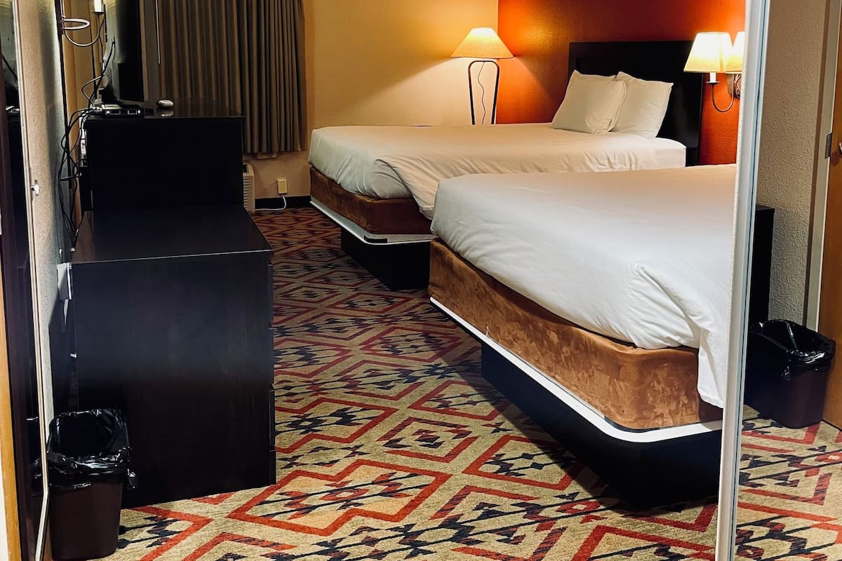 A hotel room with two beds, a desk, a TV, and a patterned carpet.