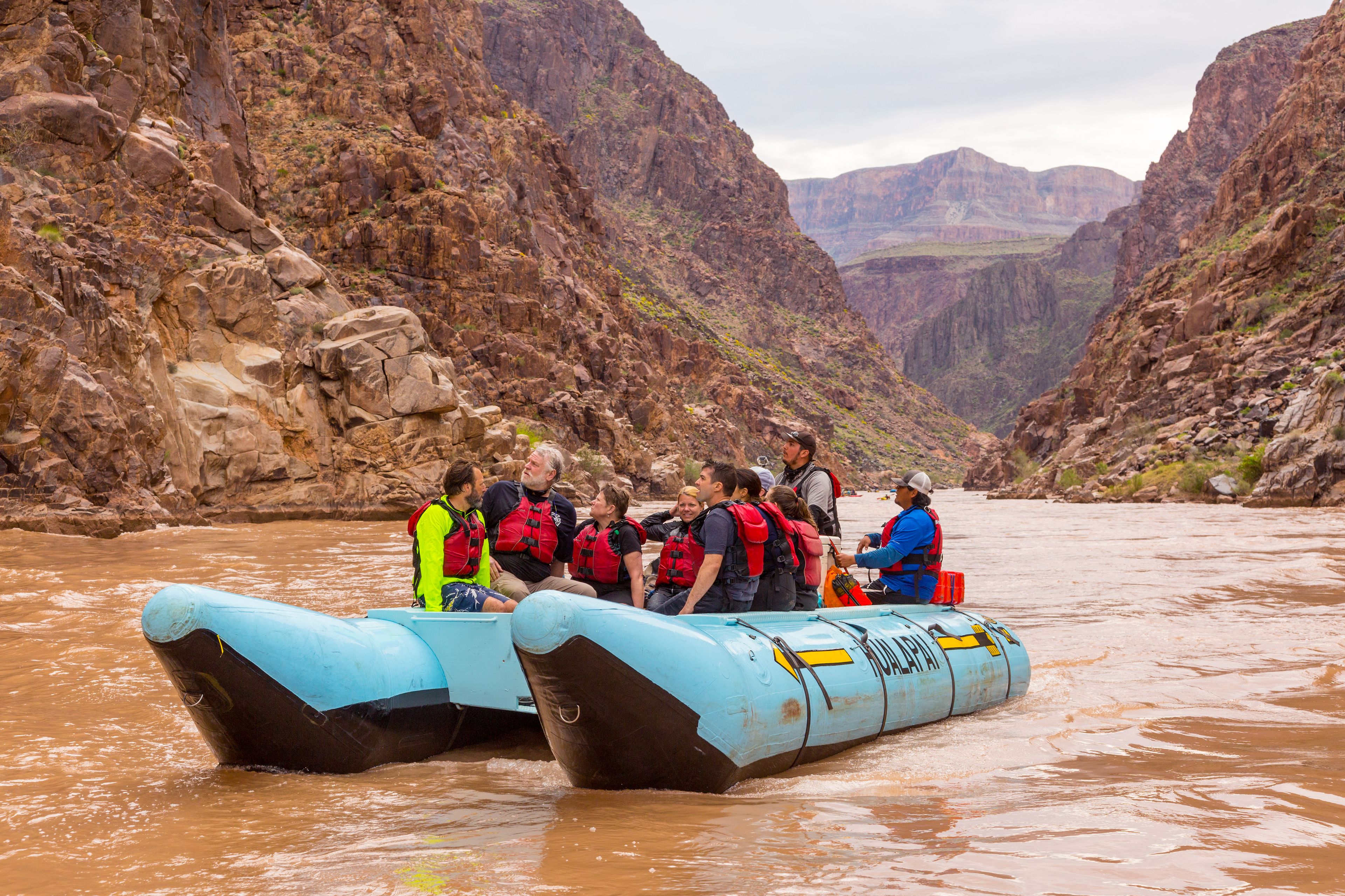 A group of people on a blue inflatable raft in a canyon with rocky cliffs.