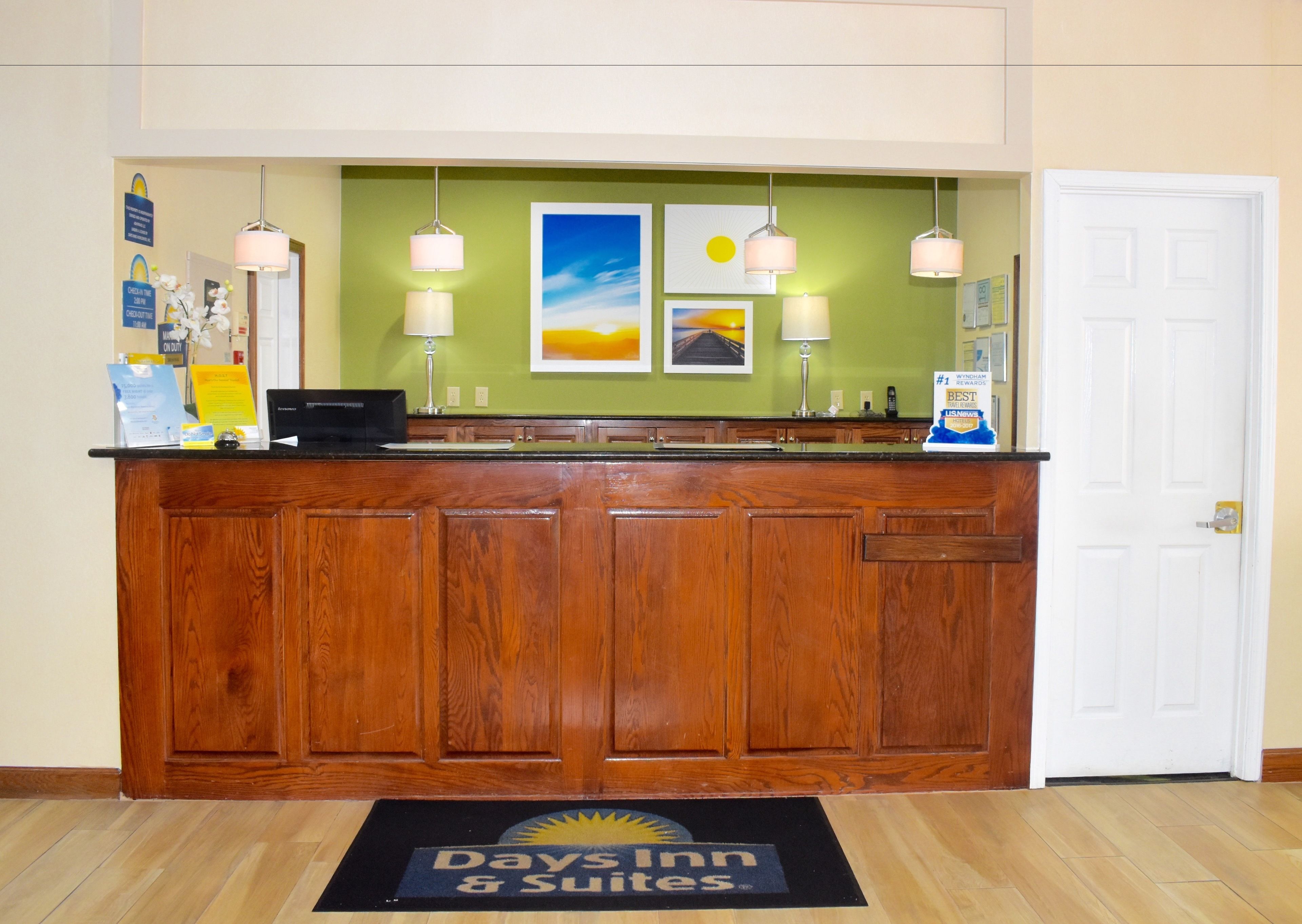 A reception desk with a wooden counter, a computer, and a sign for Days Inn & Suites.
