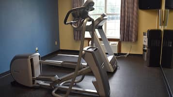 Un gimnasio con una bicicleta estática, una cinta de correr y un televisor instalado en la pared.