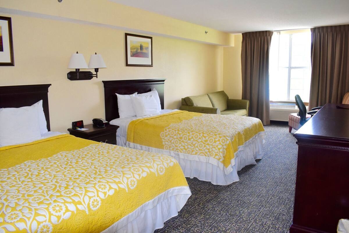 A hotel room with two beds, a desk, a chair, a lamp, and a painting on the wall.