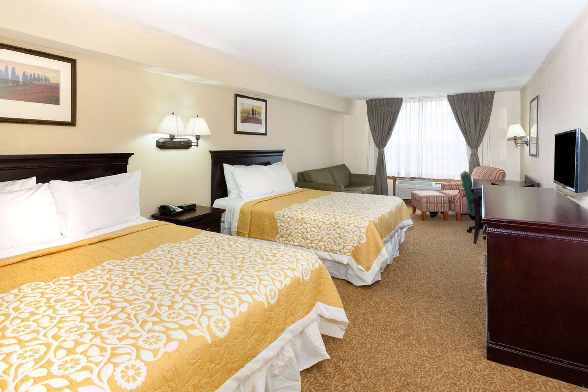 A hotel room with two beds, a desk, a chair, a TV, and a small table.