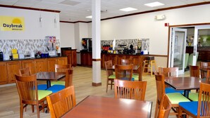 A breakfast area with wooden tables and chairs, a kitchen in the background, and a sign that reads "Daybreak Breakfast". - Days Inn & Suites by Wyndham Tucker/Northlake (Tucker)
