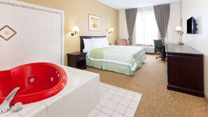 A hotel room with a red bathtub, a bed with green bedding, a desk, and a chair. - Days Inn & Suites by Wyndham Tucker/Northlake (Tucker)