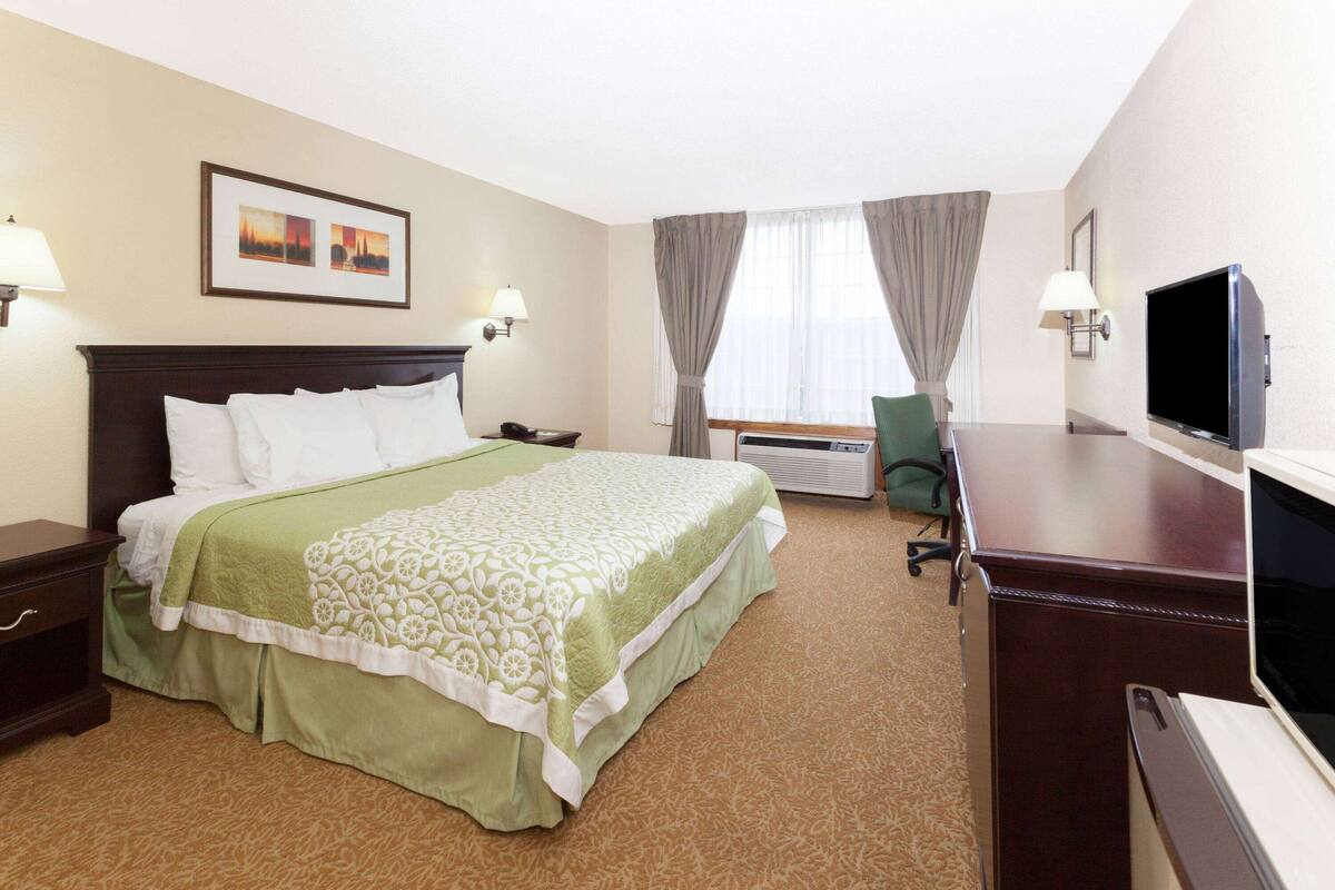 A hotel room with a large bed, a desk with a television, and a chair.