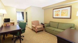A hotel room with a green armchair, a green sofa, a wooden table, and a television on a stand. - Days Inn & Suites by Wyndham Tucker/Northlake (Tucker)