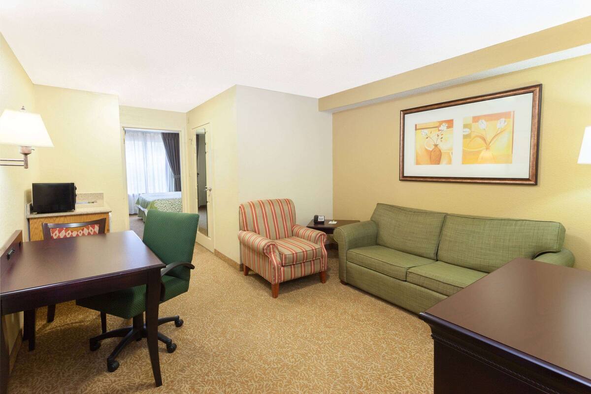 A hotel room with a green armchair, a green sofa, a wooden table, and a television on a stand.