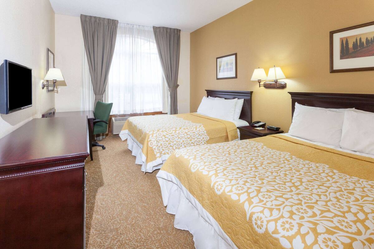 A hotel room with two beds, a desk, a chair, and a television.