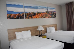 Habitación de hotel con dos camas, un cabecero de madera, una mesita de noche con lámpara y un cuadro grande con un paisaje en la pared.