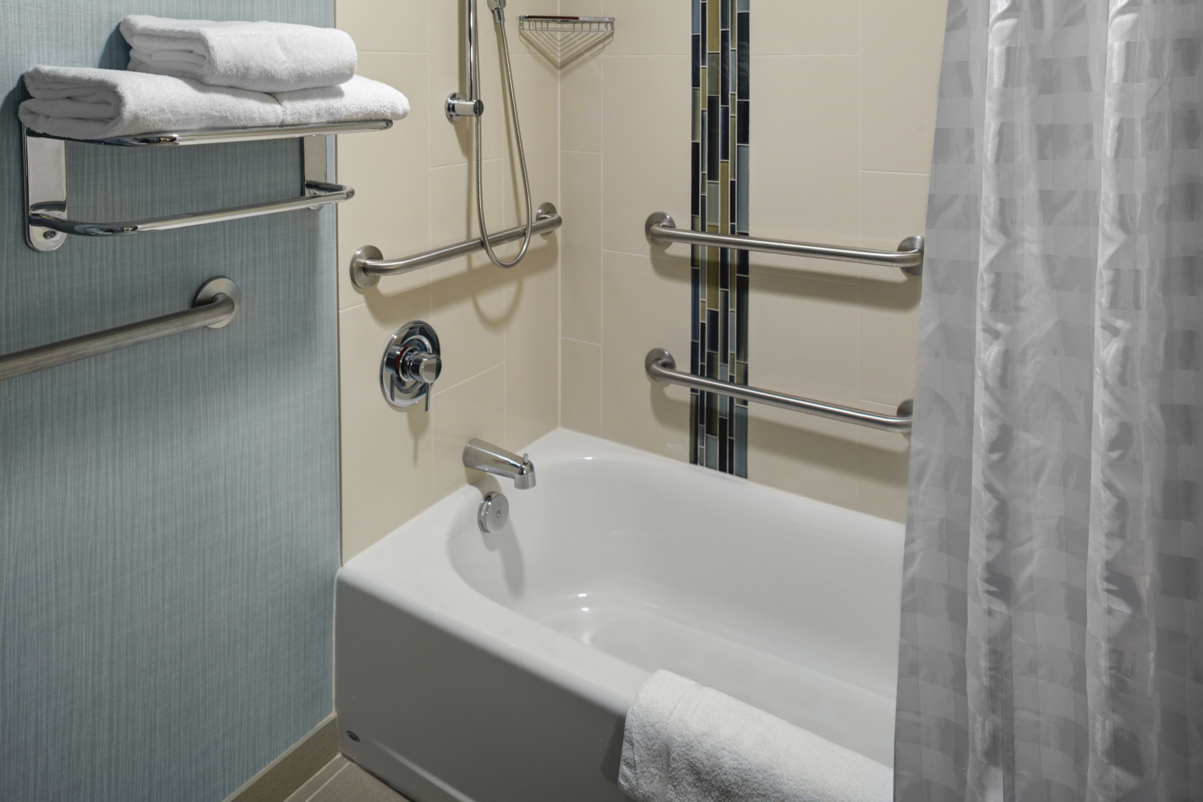 Une salle de bain équipée d’une baignoire, de barres d’appui, d’un porte-serviettes et d’un espace douche.