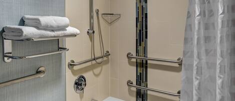 A bathroom with a bathtub, a shower with a handheld showerhead, and a towel rack with folded towels.