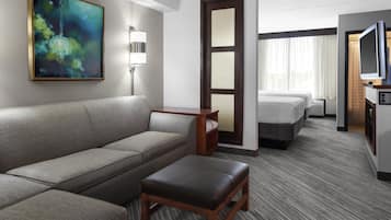 Habitación de hotel con sofá, una mesita, televisor, cama y un cuadro en la pared.