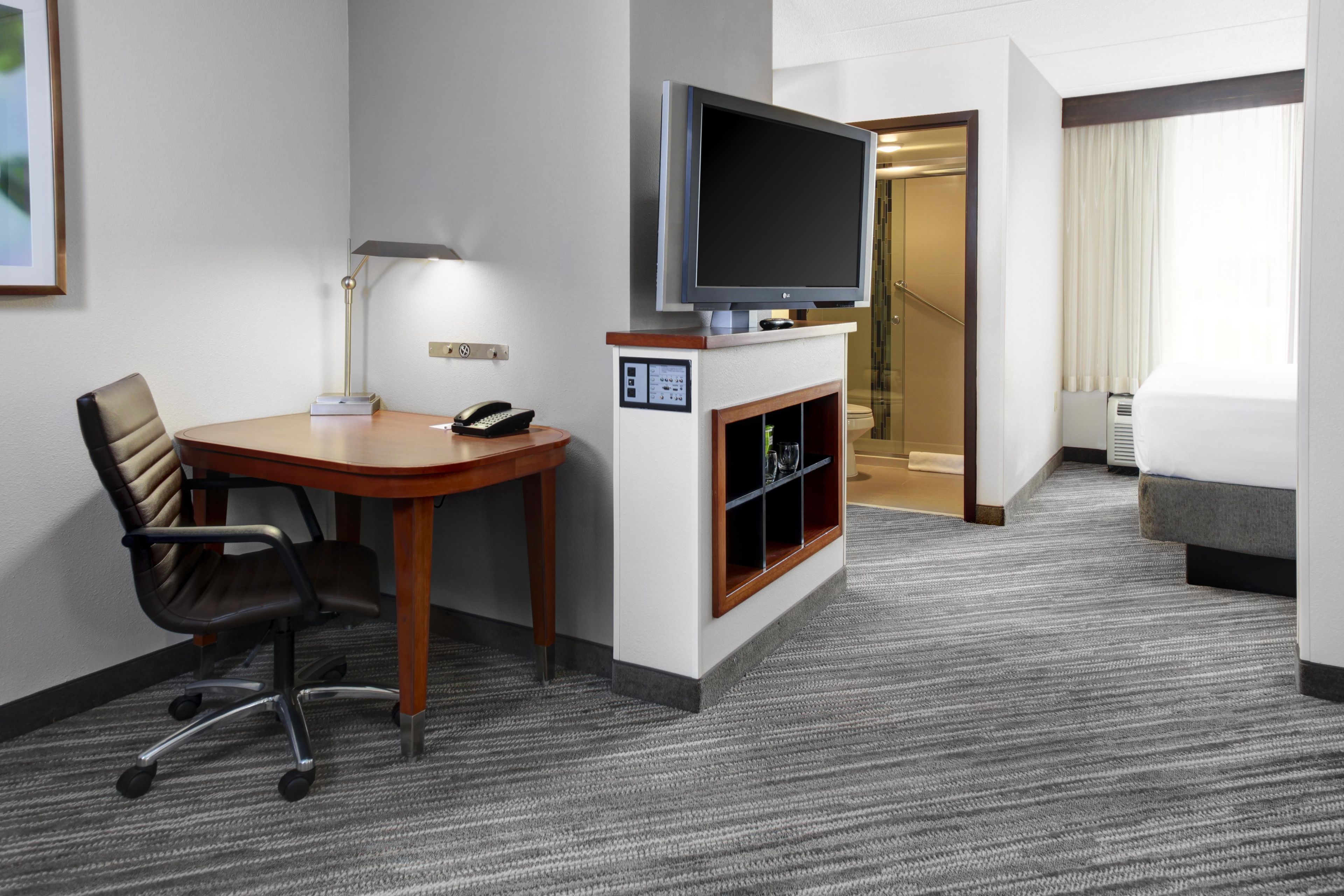 A hotel room with a desk, chair, television, and a bed.