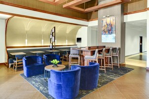 Un vestíbulo de hotel con zonas de estar, un bar y un cuadro abstracto de gran tamaño.