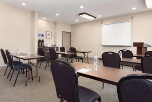 Un salón de conferencias con varias mesas y sillas, una pantalla de proyector y una estación de café.