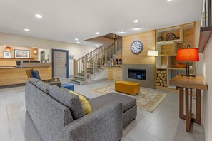 A modern living room with a grey sofa, a wooden coffee table, a fireplace, and a staircase leading to an upper floor. - Country Inn & Suites by Radisson Romeoville I-55 (Romeoville)