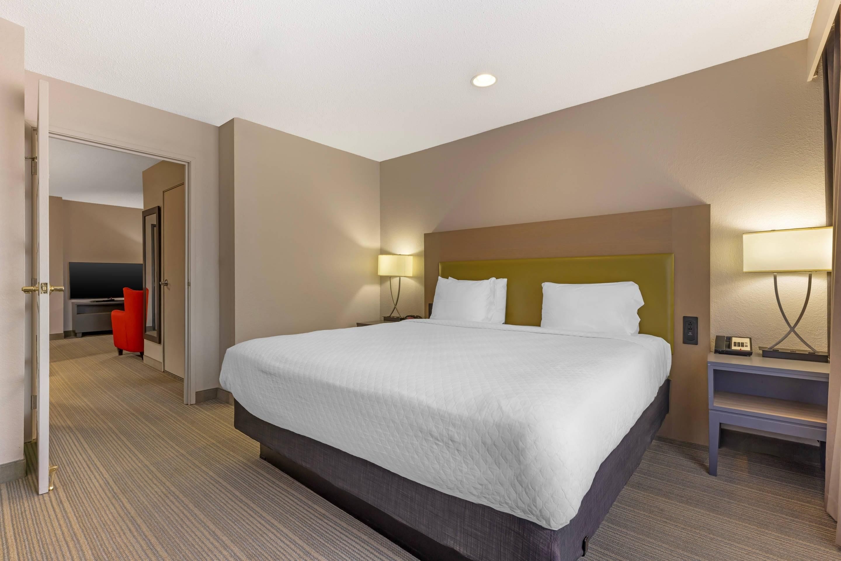 A hotel room with a large bed, bedside lamps, a TV, and a red chair.