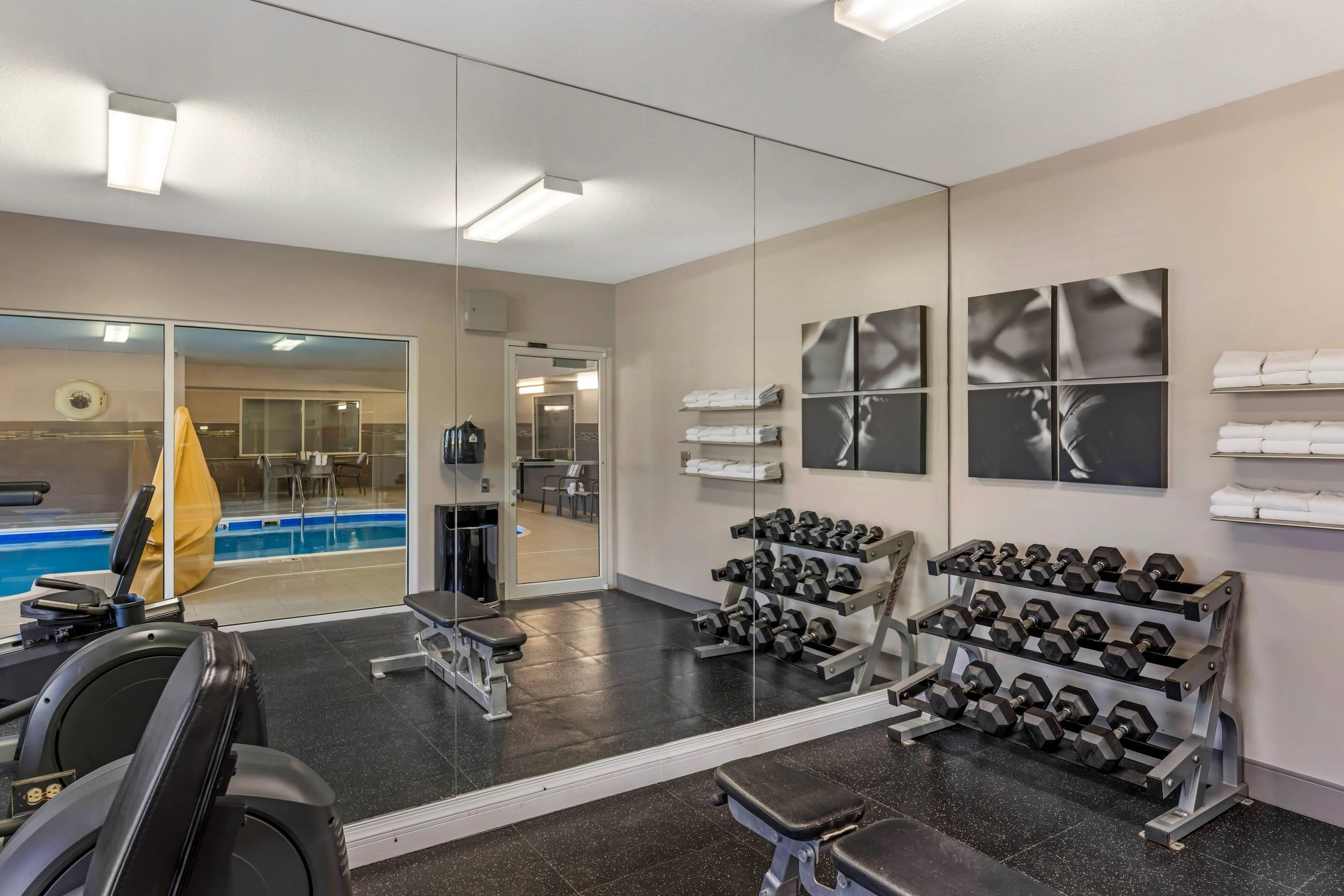 A gym with exercise equipment, a mirror, and a pool area visible through the glass doors.