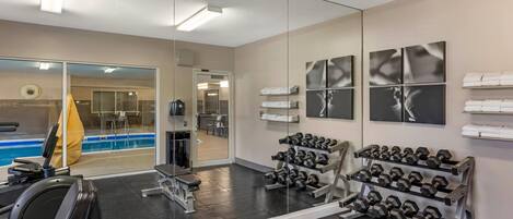 A gym with exercise equipment, a mirror, and a pool area visible through the glass doors.