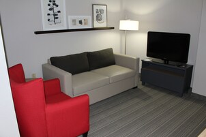 Una sala de estar moderna con un sofá, un sillón rojo, un televisor y una lámpara.