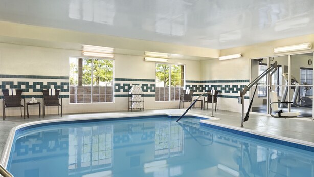 A swimming pool with a tiled border, sunlit interior, and a view of the outdoors through large windows.