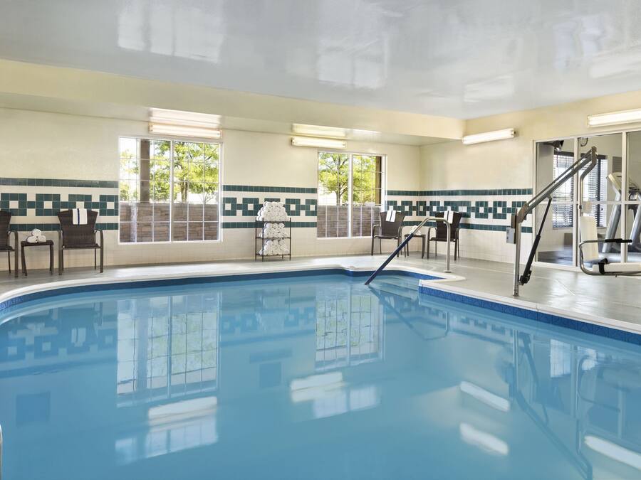 Piscina com borda azulejada, interior iluminado pelo sol e vista para o exterior através de grandes janelas.