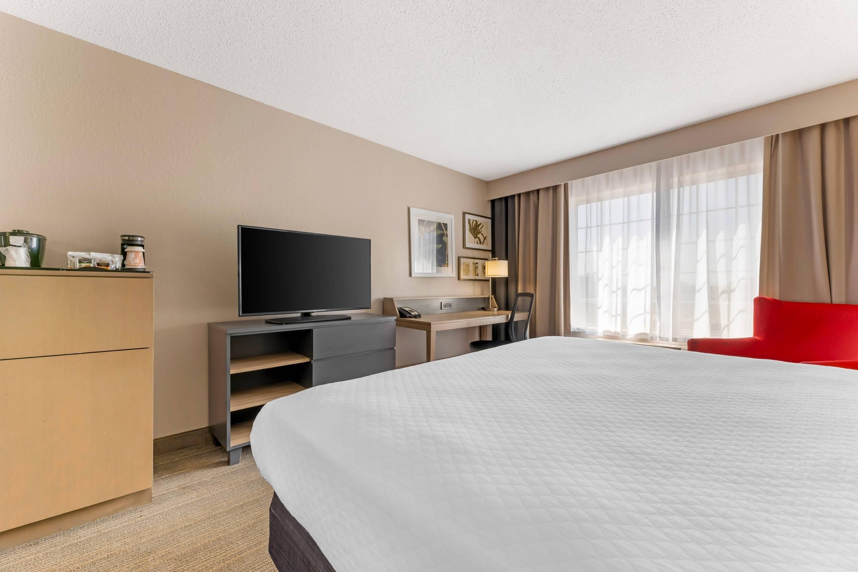 Quarto de hotel com cama, escrivaninha, televisão e cadeira.