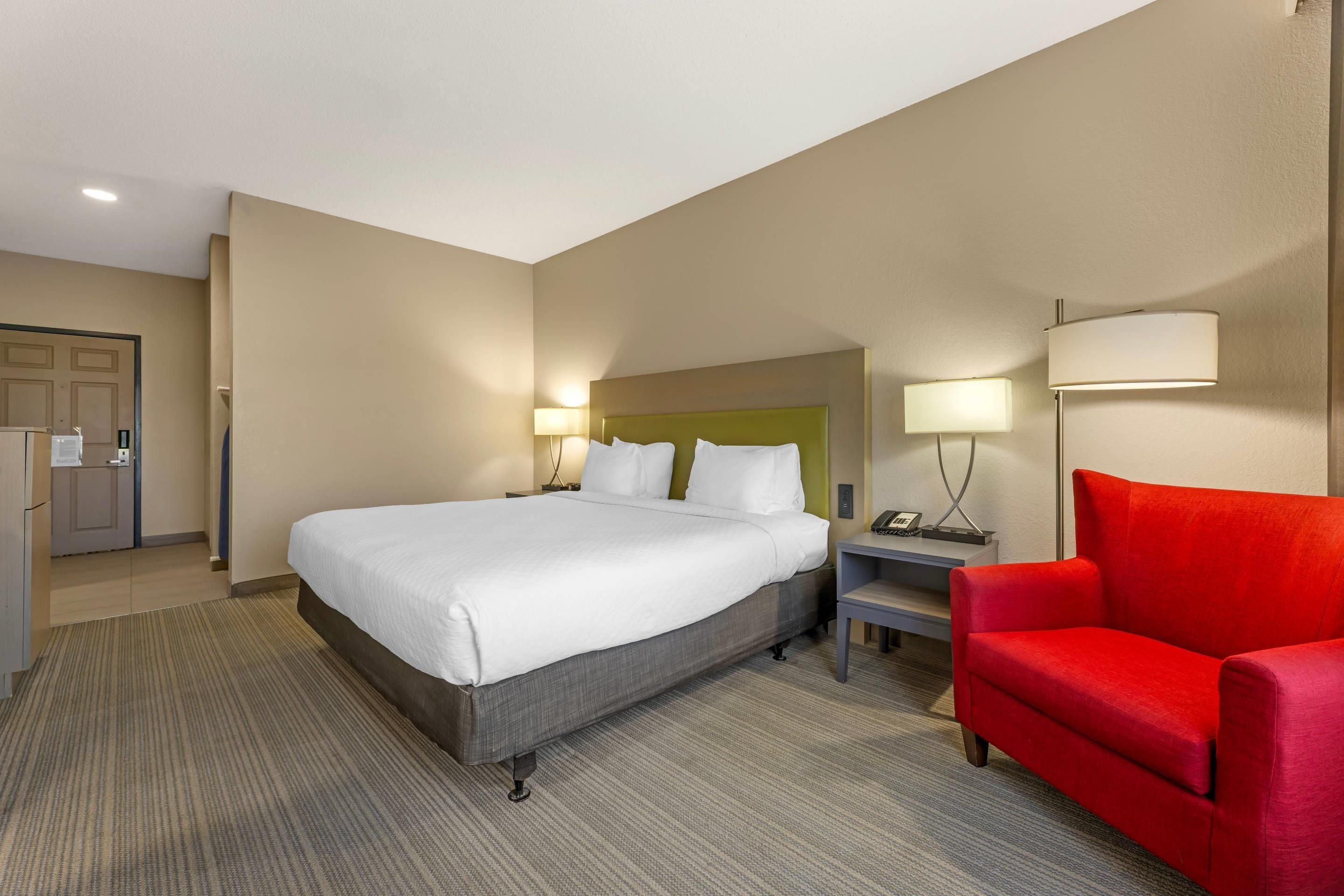 Une chambre d’hôtel avec un grand lit, un fauteuil rouge, une table de chevet avec une lampe et un téléphone.