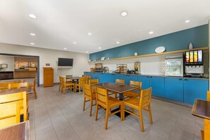 A modern restaurant with blue cabinets, wooden tables and chairs, and a self-service beverage station.