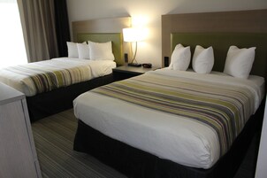 Una habitación de hotel con dos camas, cada una con una colcha a rayas, una mesita de noche con lámpara y un cabecero.