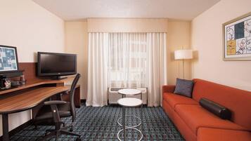 A hotel room with a desk, television, sofa, and a patterned carpet.
