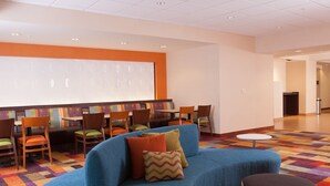 A modern lounge area with a blue sofa, patterned cushions, and a projector screen on the wall. - Fairfield Inn by Marriott Greenville-Spartanburg Airport (Greenville)