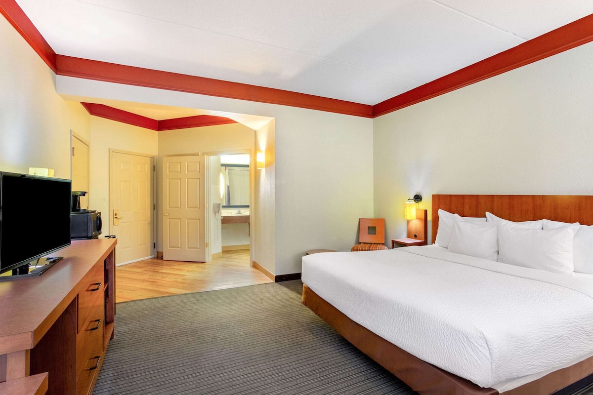 A hotel room with a large bed, a TV on a wooden dresser, and a bathroom visible through an open door.