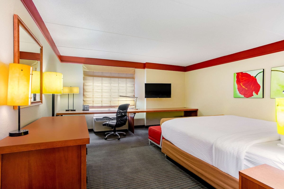 A hotel room with a bed, desk, chair, and a TV on the wall.