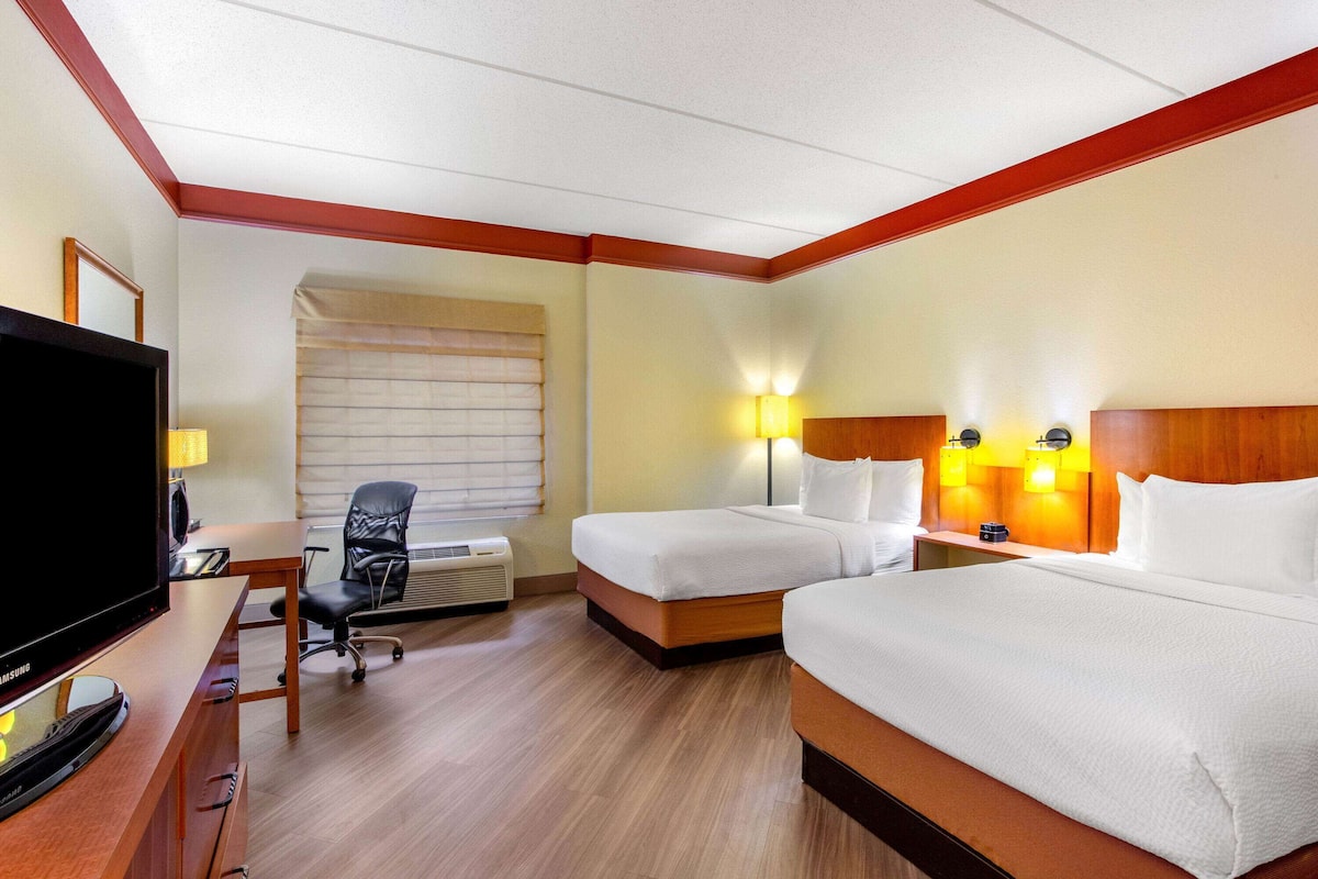 A hotel room with two beds, a desk with a TV, a chair, and a window with blinds.