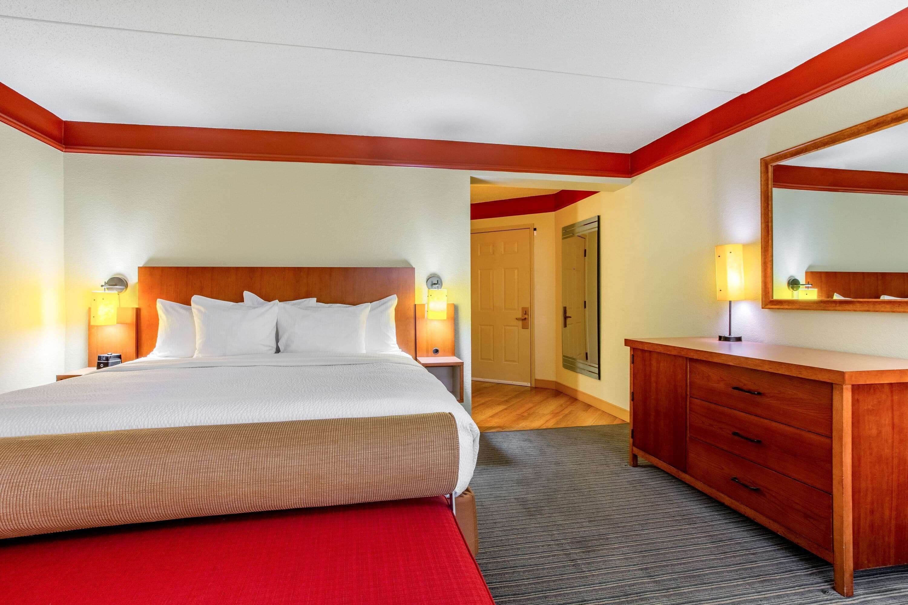 Een hotelkamer met een groot bed, een houten hoofdbord, twee bedlampen, een houten dressoir en een spiegel.