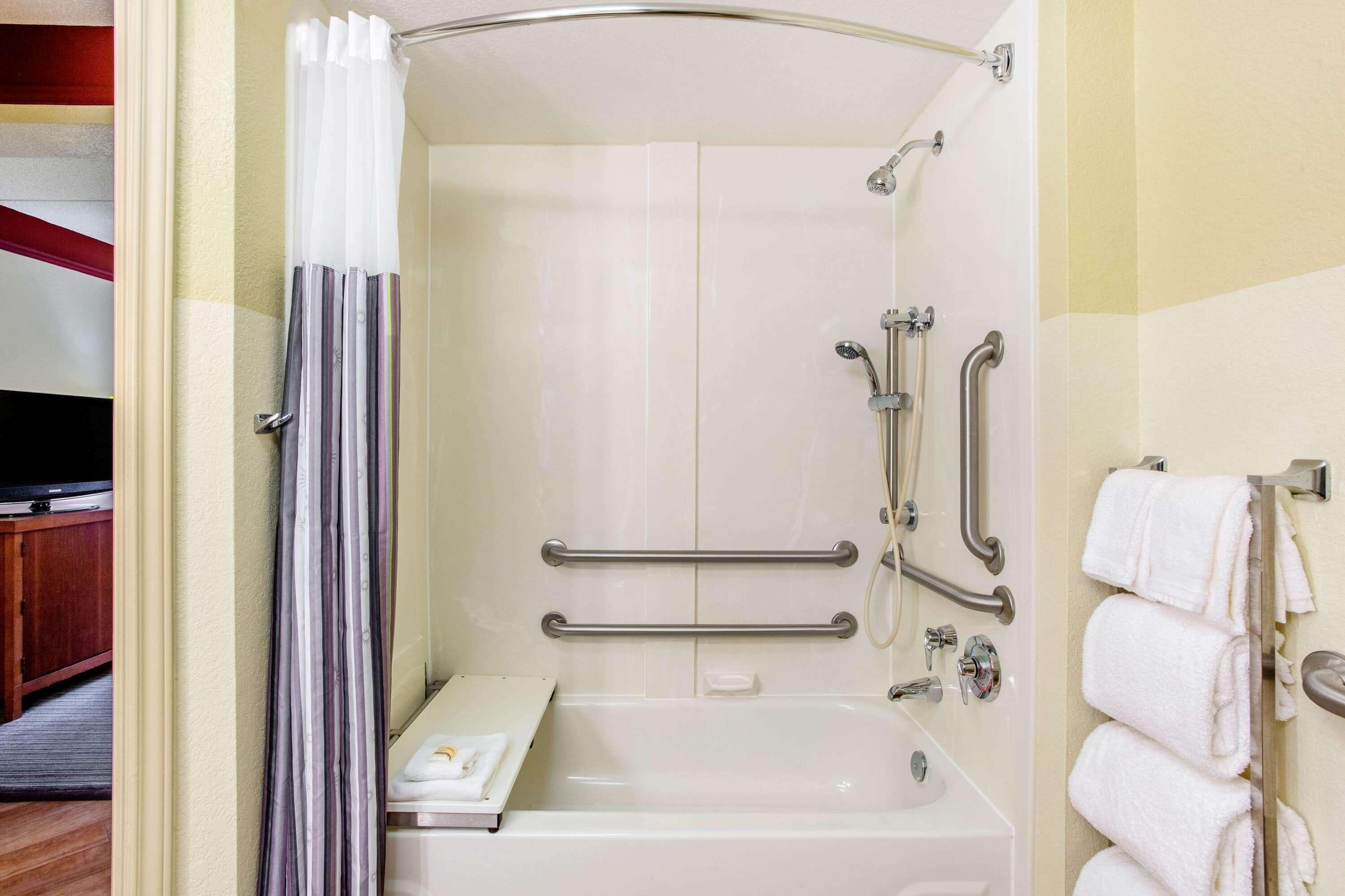 A bathroom with a walk-in shower, grab bars, a towel rack, and a toilet with a raised seat.