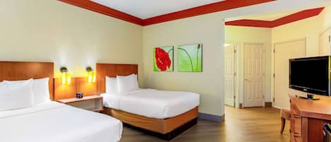 A hotel room with two beds, wooden headboards, bedside lamps, a flat-screen TV, and artwork on the wall.