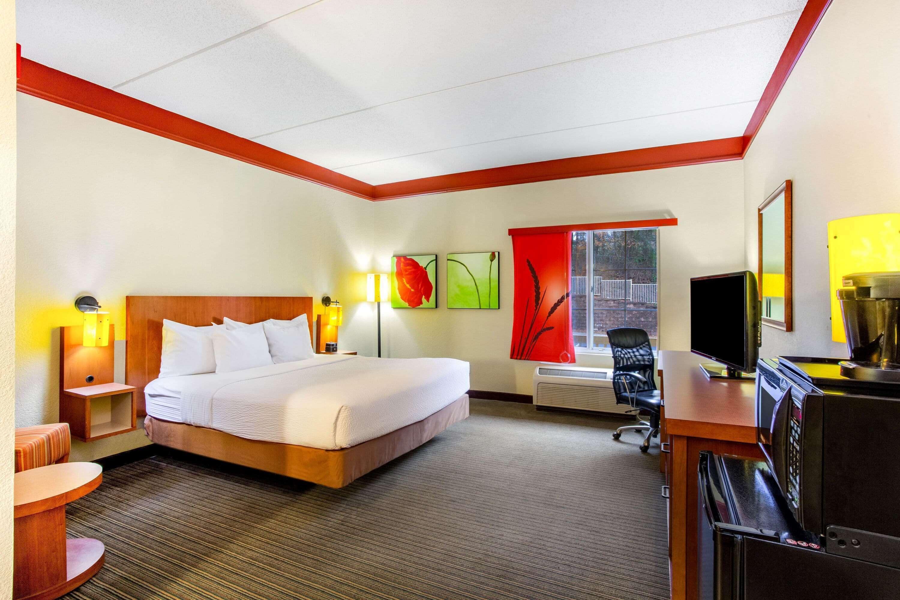 A hotel room with a bed, desk, chair, and a window with a view.
