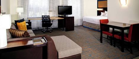 A hotel room with a bed, a desk with a TV, a sofa, and a small table.