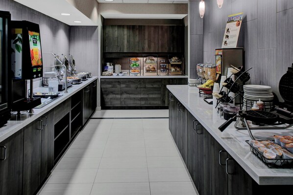 A modern breakfast bar with self-service stations, including a coffee machine, fruit, and pastries.
