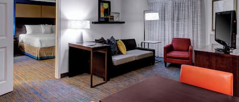Una habitación de hotel con cama, sofá, escritorio, silla, televisor y lámpara.