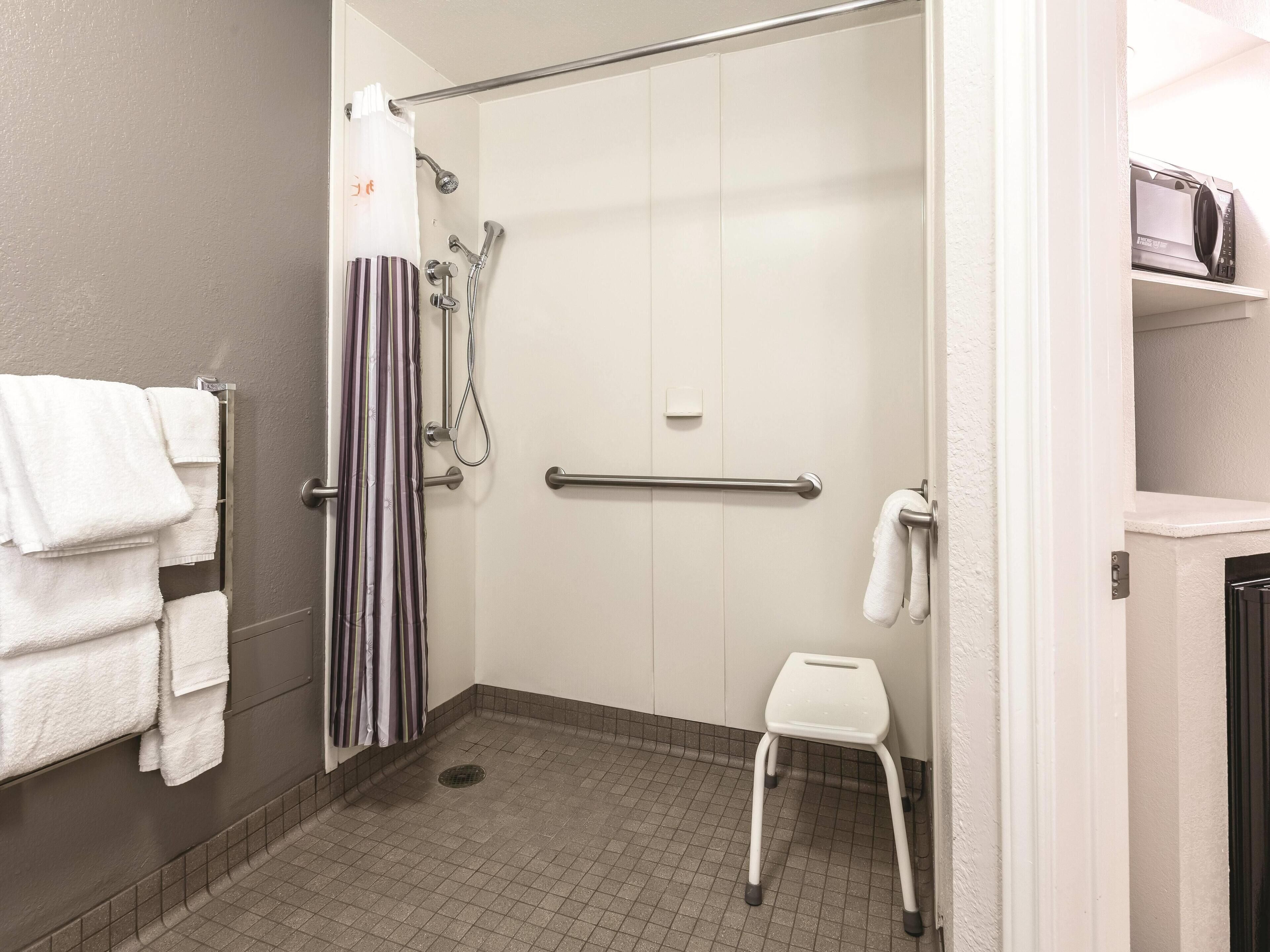 A shower area with a grab bar, a white towel rack, a striped shower curtain, and a white step stool.